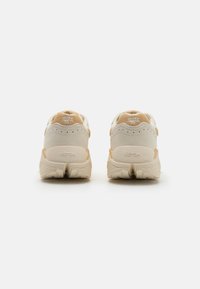 Beige and cream sneakers with suede and mesh materials, featuring a textured sole, visible branding, and padded ankle collars.