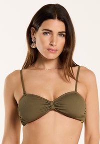 Aliejinės žalios spalvos bikini viršus su reguliuojamomis plonomis petnešėlėmis, susiraukšlėjęs centrinis dizainas ir subtilus tekstūruotas audinys. Yra šoninės susiraukšlėjimai ir auksinės detalės akcentas.