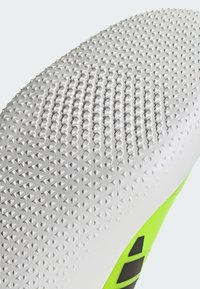 Podošva topánky s textúrovaným povrchom vyrobená z bielej gumy, s malými trojuholníkovými vzormi a jasne zeleným akcentom na boku.