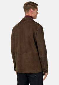 Brun mockaskinnjacka med urtagna kragar, texturerad yta och knäppte manschetter. Har en rak skärning och minimalistiska designelement.