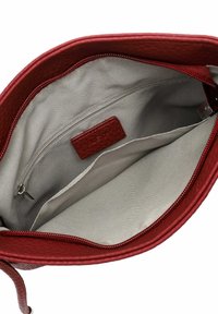 Intérieur d'un sac à main en cuir rouge avec une doublure beige lisse, une poche zippée et une étiquette. Le design met en avant l'espace et l'organisation.