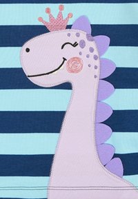 Design di un dinosauro viola su un tessuto a righe blu navy e azzurro chiaro, con una corona, espressione sorridente e dettagli di texture cuciti.
