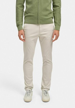 Lys beige slim-fit bukser med en glat tekstur, parret med en grøn tekstureret lynlås cardigan og lysegrå sneakers.