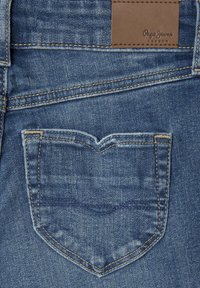 Modré džínsy s klasickým dizajnom, vybavené vreckom na chrbte v tvare srdca a hnedou koženou nálepkou s nápisom "Pepe Jeans London."