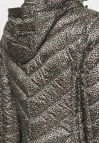 Veste matelassée avec un motif léopard en marron, beige et noir. Comprend une capuche et un design de matelassage diagonal.