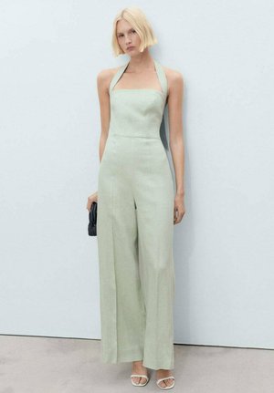 Jumpsuit in lino verde chiaro con scollo quadrato e spalline al collo. Design a gamba larga, abbinato a una clutch nera e scarpe bianche.