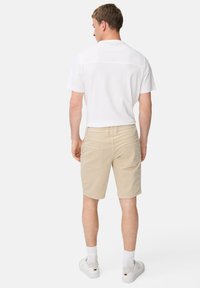 Weißes T-Shirt mit kurzen Ärmeln, beige Shorts mit zwei Gesäßtaschen und weiße Sneaker mit kontrastierenden Akzenten. Glattes Material mit lässigem Schnitt.
