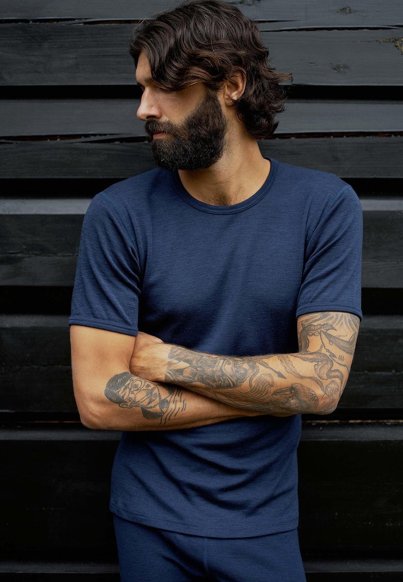 Marineblå kortærmet t-shirt lavet af blødt stof, med rund halsudskæring og en afslappet pasform, båret af en mand med tatoverede arme.