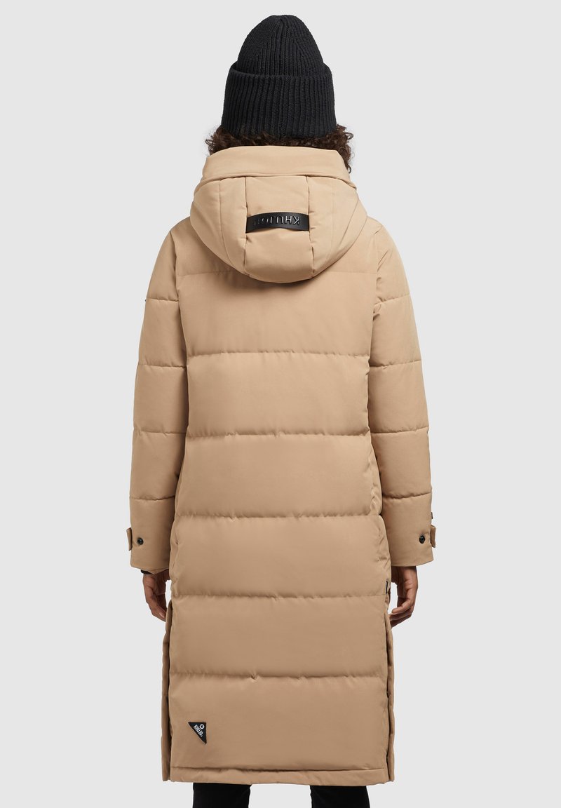 Long manteau en duvet beige avec capuche, design matelassé horizontal, étiquette de marque noire à l'arrière et poignets ajustables.