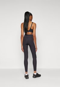 Black sports bra and leggings made from stretchy fabric. The leggings feature a high waist and small perforations on the lower legs. Black sneakers.