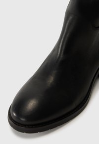 Bottine en cuir noir à bout rond, texture lisse et semelle robuste. Présente des coutures minimales et un design élégant.