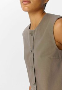 Mouwloos grijs linnen vest met een ronde hals, knoopsluiting aan de voorkant en zijzak, met een gladde textuur en minimalistisch ontwerp.