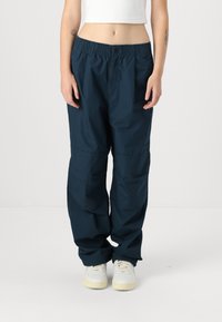 Pantaloni in tessuto leggero di colore blu navy, con vita elastica, fit morbido e tasche laterali, indossati con sneakers bianche.