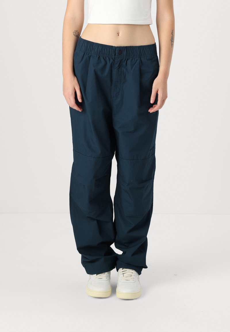 Pantaloni in tessuto leggero di colore blu navy, con vita elastica, fit morbido e tasche laterali, indossati con sneakers bianche.