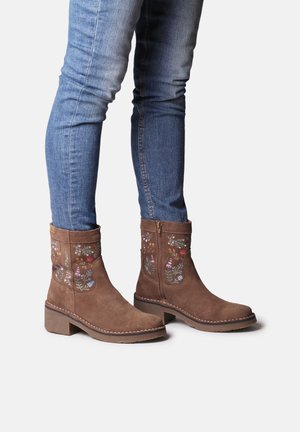Bruine suède enkelboots met bloemenborduursel aan de zijkanten, ronde neus, blokhak en een rits aan de zijkant voor gemakkelijke instap.