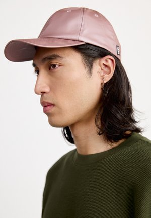 Casquette en cuir rose avec un bord courbé, des coutures détaillées et une sangle réglable, associée à une chemise verte olive texturée.