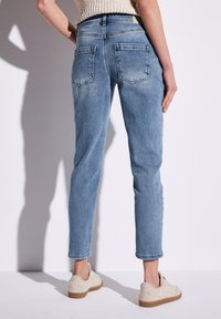 Světlé modré džíny s tapered střihem, které mají dvě zadní kapsy a jemné vyblednutí. V kombinaci s krémovými teniskami.