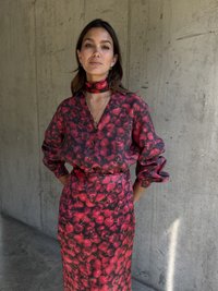 Tištěná květinová blůza a odpovídající sukně v odstínech červené a růžové. Blůza má ohrnuté rukávy; šátek ladí s outfitem s květinovým vzorem.