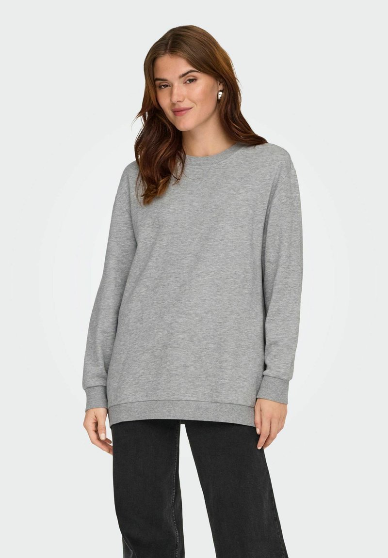 Sudadera de felpa gris con cuello redondo, mangas largas y puños y dobladillo acanalados. La lleva con pantalones negros de corte relajado.
