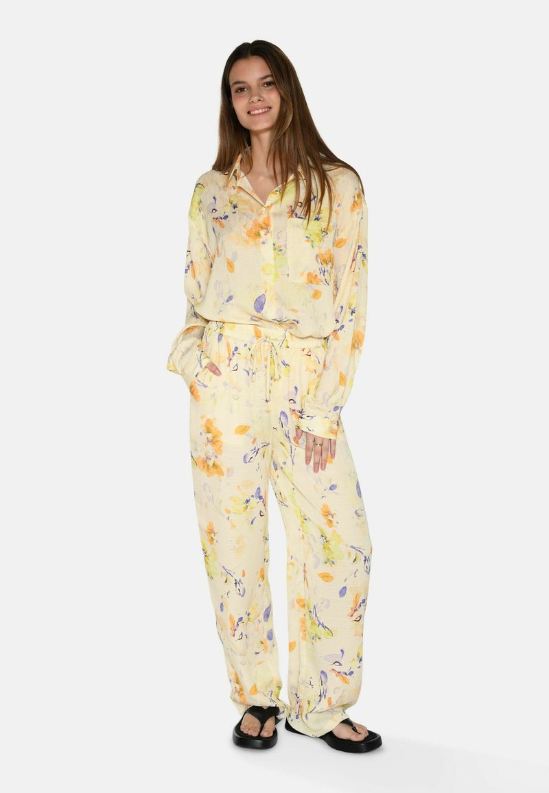 Ensemble de pyjama floral jaune, avec des motifs orange et violet. Coupe ample, chemise à bouton avec manches longues et pantalon à taille élastique.