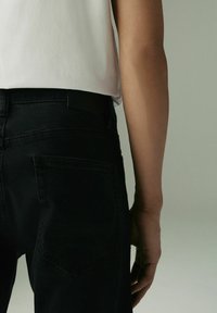 Zwarte denim jeans met een slim fit ontwerp, voorzien van achterzakken en een gladde textuur, gedragen met een eenvoudig wit t-shirt.