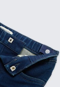 Blauwe spijkerbroek, voorzien van een metalen drukknoop en knoopsluiting, met textuurstof en een licht vervaagde tailleband voor extra detail.