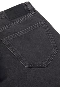 Jeans de denim negro con un bolsillo trasero, sutilezas en las costuras y una etiqueta de cuero en la cintura. Tejido texturizado, diseño casual.