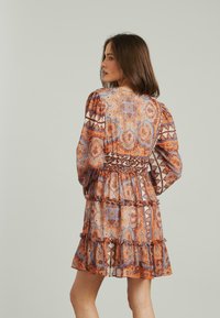 Kurzärmliges, gemustertes Kleid in Orange, Blau und Creme mit Rüschensaum und geraffter Taille, das Paisley- und geometrische Designs zeigt.