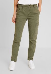 Oliwkowe spodnie cargo o wąskim kroju, z bocznymi kieszeniami, kieszeniami z przodu oraz zapięciem na guzik. W zestawie z białymi trampkami.
