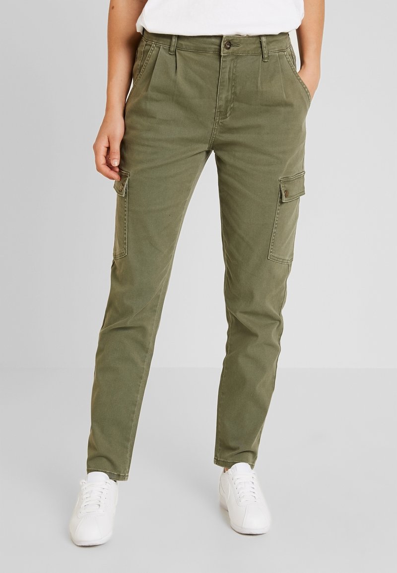 Oliwkowe spodnie cargo o wąskim kroju, z bocznymi kieszeniami, kieszeniami z przodu oraz zapięciem na guzik. W zestawie z białymi trampkami.