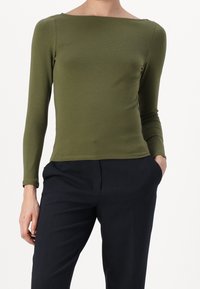 Olivgrön långärmad topp i en figurnära design med båthals, tillverkad av mjukt, elastiskt tyg. Matchas med mörkblåbyxor.