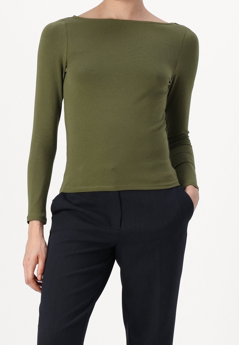 Olivgrön långärmad topp i en figurnära design med båthals, tillverkad av mjukt, elastiskt tyg. Matchas med mörkblåbyxor.