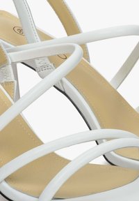 Witte sandalen met banden die een gladde beige binnenzool hebben, dunne banden met een gekruisd ontwerp en een elegante zwarte buitenzool.
