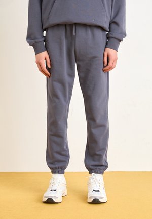 Grey sweatpants made of cotton, featuring an elastic waistband and cuffs, paired with white athletic shoes with blue accents.