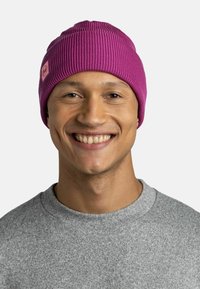 Purple ribbed knit beanie with a textured finish and a small logo patch, worn by a person in a gray sweatshirt, against a light background.