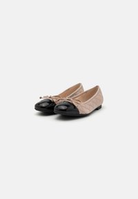 Ballerine con superiore beige trapuntato e punta in vernice nera lucida. Presentano un piccolo fiocco sulla parte anteriore e un tacco basso e piatto.
