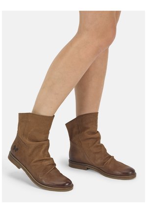 Bruine leren laarzen tot halverwege de kuit met een lage hak, gedragen op blote benen, met een licht ingezakte look en een klein donker vlinderlogo bij de hiel.