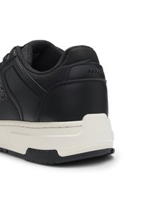 Svart sneaker med en teksturert læroverdel, med polstret krage, hvit mellomsole og gummisåle med grep-mønster.