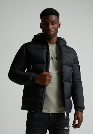 Black puffer jacket with a hood, zippered pockets, and elastic cuffs, worn over a light green shirt, paired with dark jeans.