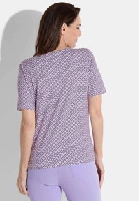 Haut violet à manches courtes avec un motif en losange, conçu en tissu doux avec une coupe décontractée, porté avec un pantalon lavande clair.