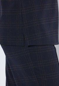 Pantaloni sartoriali blu navy con motivo a quadri, caratterizzati da una texture liscia, tasche laterali e cuciture a contrasto nei toni del marrone e dell'arancio.
