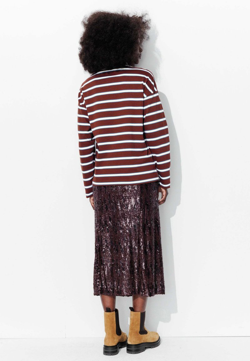 Haut à manches longues rayé marron et bleu associé à une jupe brillante et pailletée, longueur genou. Porté avec des bottes Chelsea beige.