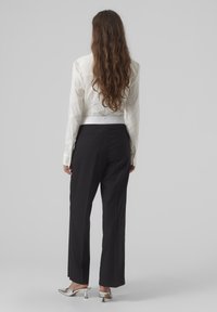 Chemise blanche à manches longues associée à un pantalon large noir. Le pantalon présente une texture lisse et une coupe classique. Des talons argentés complètent le look.