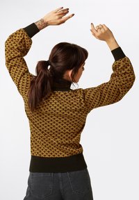 Pull en tricot à motifs marron et or avec manches bouffantes, col et ourlet côtelés. Le design texturé comporte des formes de diamant.