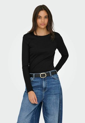 Schwarzes langärmliges, geripptes Oberteil, kombiniert mit hochgeschnittenen, blauen Jeans mit weitem Bein und einem schwarzen Gürtel mit goldener Schnalle.