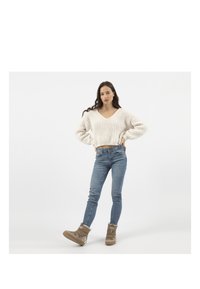 Pull en tricot épais crème avec un décolleté en V, associé à un jean skinny bleu clair et des bottes d'hiver beiges. Design simple et texturé.