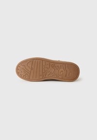 Suela de un zapato marrón con patrones de agarre de goma texturizada que incluyen líneas y formas abstractas, fotografiada sobre un fondo blanco.