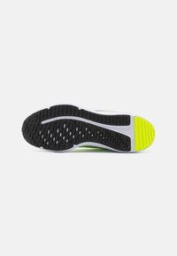 Black rubber outsole with textured grip patterns, white midsole, and bright yellow accent on the heel. Ergonomic, flexible design.