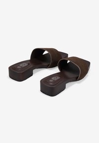 Sandalias tipo slide marrón oscuro con tiras anchas de ante, punteras cuadradas abiertas y tacones bajos de bloque sobre un fondo blanco.