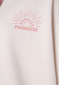 Felpa beige chiaro con un design grafico rosa che presenta il testo "SUNRISE PARADISE" e dettagli di raggi di sole. Tessuto morbido.